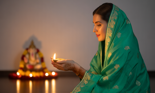 A woman applying Glamacious skincare products for Ganesh Festival glow, surrounded by festive decor